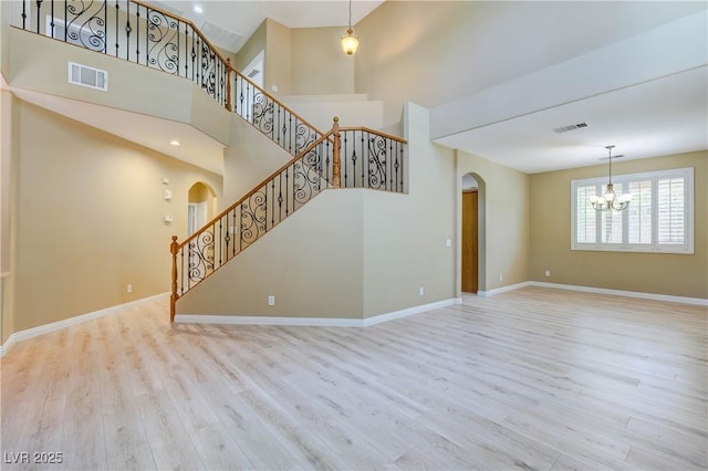 11478 Bargetto Ct, Las Vegas, NV 89141 - unfurnished living room featuring arched walkways, wood finished floors, a chandelier, baseboards, and a towering ceiling
