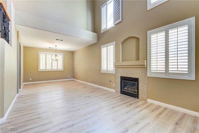 11478 Bargetto Ct, Las Vegas, NV 89141 - unfurnished living room with a chandelier, wood finished floors, a tiled fireplace, baseboards, and a towering ceiling