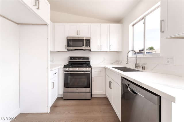 5751 Mabel Rd, Las Vegas, NV 89110 - kitchen with stainless steel appliances, a sink, lofted ceiling, light wood-style flooring, and white cabinetry