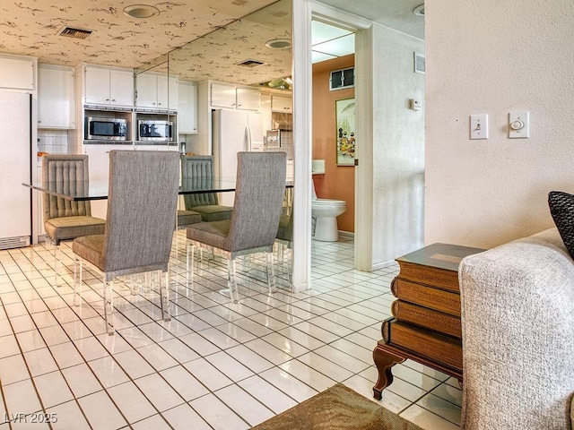 940 Vegas Valley Dr, Las Vegas, NV 89109 - kitchen featuring stainless steel microwave, white refrigerator, freestanding refrigerator, light tile patterned floors, and a textured wall