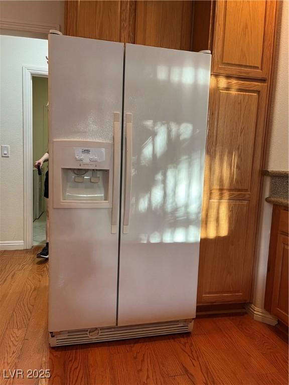 5049 Alfingo St, Las Vegas, NV 89135 - kitchen view of white fridge with ice dispenser, light wood-style floors, brown cabinets, and baseboards