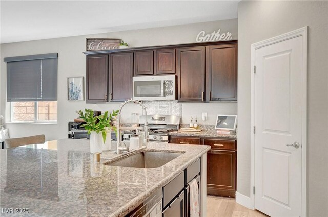 kitchen featuring appliances with stainless steel finishes, light stone counters, dark brown cabinets, and light wood-type flooring