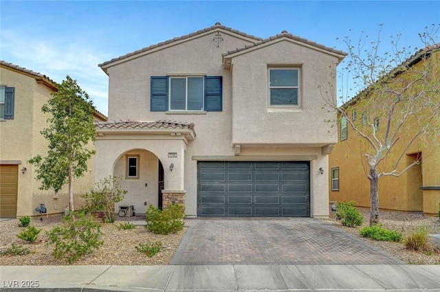 mediterranean / spanish home with stucco siding, a tiled roof, an attached garage, and decorative driveway
