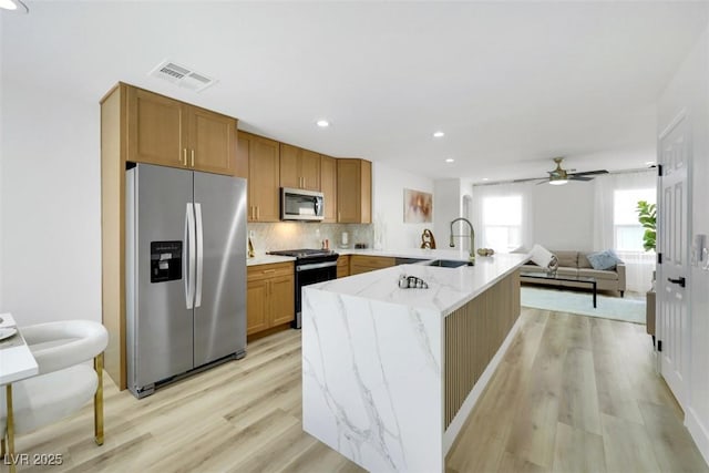 9078 Hilverson Ave, Las Vegas, NV 89148 - kitchen with stainless steel appliances, a peninsula, light stone counters, light wood-type flooring, and a sink