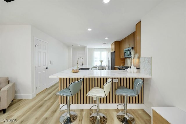 9078 Hilverson Ave, Las Vegas, NV 89148 - kitchen featuring appliances with stainless steel finishes, brown cabinets, light wood-type flooring, recessed lighting, and a peninsula
