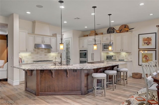 748 Puerto Real Ct, Las Vegas, NV 89138 - kitchen with under cabinet range hood, built in appliances, a sink, decorative backsplash, and light wood finished floors