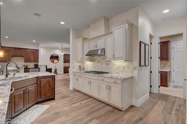 748 Puerto Real Ct, Las Vegas, NV 89138 - kitchen with a sink, under cabinet range hood, light wood-style floors, backsplash, and baseboards
