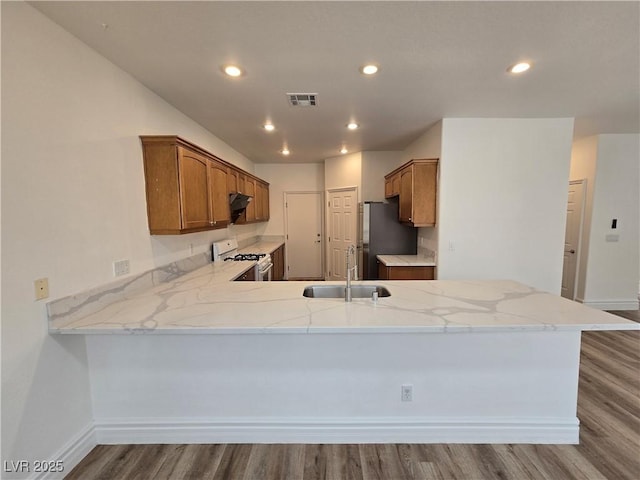 6638 Babys Tear Pl, Las Vegas, NV 89148 - kitchen with white gas range oven, a sink, freestanding refrigerator, a peninsula, and wood finished floors