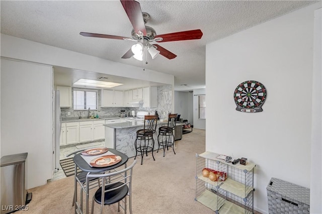6735 W Charleston Blvd Unit 4, Las Vegas, NV 89146 - kitchen with a peninsula, a sink, a kitchen breakfast bar, light carpet, and white cabinets