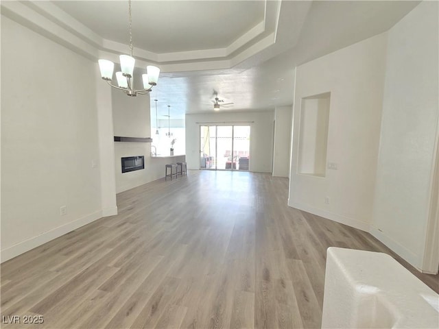 8545 Summer Vista Ave, Las Vegas, NV 89145 - unfurnished living room featuring a tray ceiling, a chandelier, light wood-style floors, and baseboards