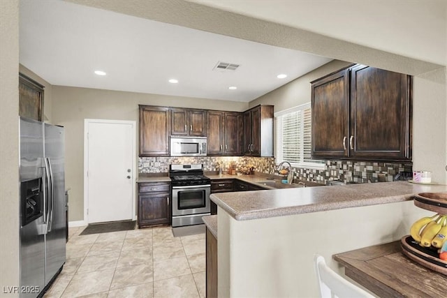 8015 Maple Park St, Las Vegas, NV 89131 - kitchen featuring appliances with stainless steel finishes, a peninsula, a sink, dark brown cabinets, and decorative backsplash