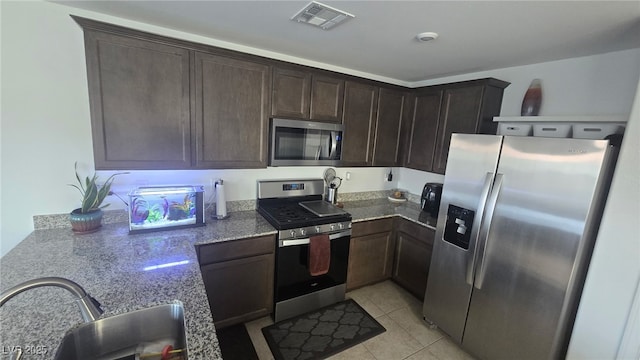 5209 Silica Chalk Ave, Las Vegas, NV 89115 - kitchen with stainless steel appliances, dark brown cabinetry, light tile patterned flooring, and stone counters