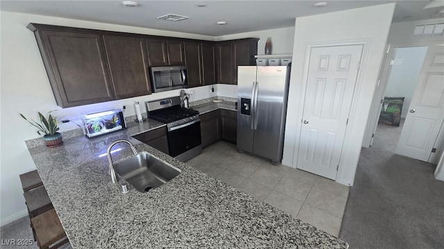 5209 Silica Chalk Ave, Las Vegas, NV 89115 - kitchen featuring stainless steel appliances, a peninsula, dark stone counters, dark brown cabinets, and light tile patterned flooring