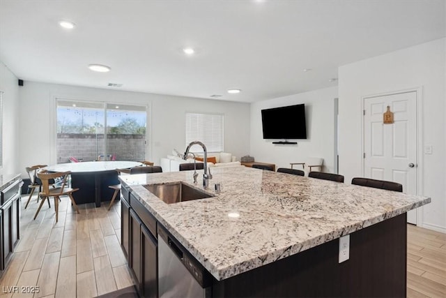 7616 Quail Dust St, North Las Vegas, NV 89084 - kitchen featuring stainless steel dishwasher, a sink, light wood finished floors, light stone counters, and a kitchen island with sink