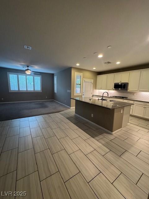 4108 Fairywren Dr, North Las Vegas, NV 89031 - kitchen with stainless steel microwave, white cabinetry, open floor plan, a sink, and decorative backsplash