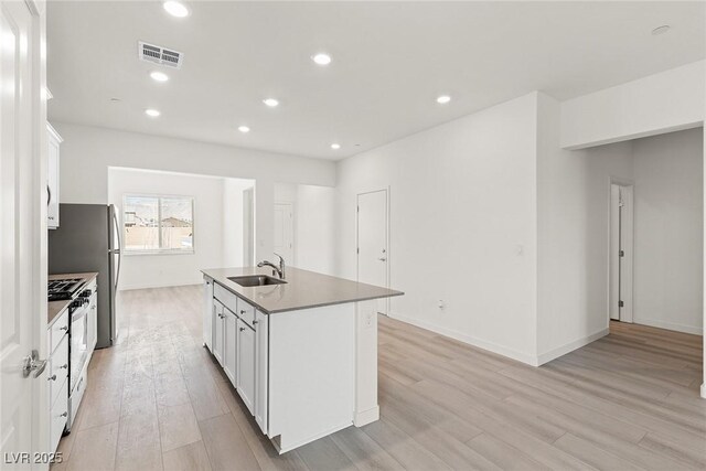 2751 Avril Point St, Las Vegas, NV 89156 - kitchen with gas range, a sink, light wood-type flooring, a kitchen island with sink, and white cabinets