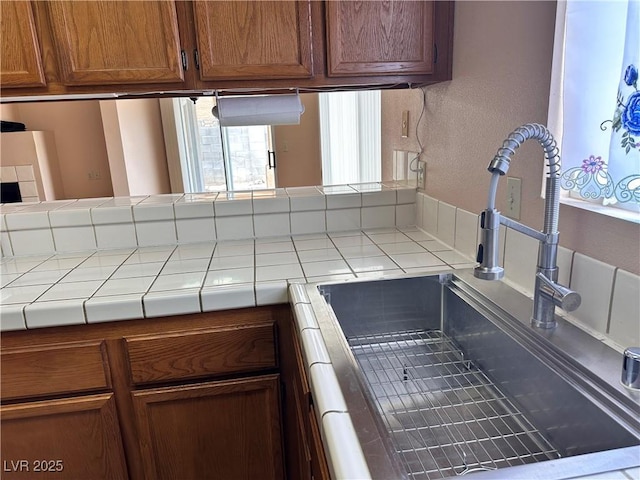 6600 Silver Penny Ave, Las Vegas, NV 89108 - kitchen featuring tile counters, a sink, brown cabinets, and a textured wall
