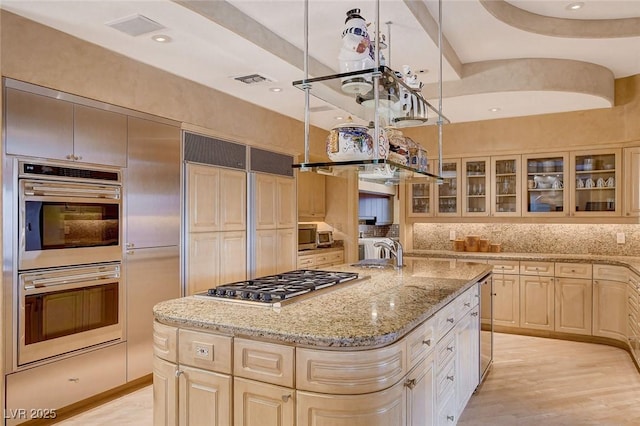 60 Innisbrook Ave, Las Vegas, NV 89113 - kitchen with stainless steel appliances, a sink, light brown cabinets, a center island with sink, and glass insert cabinets