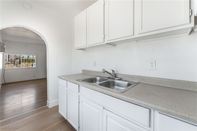 517 N 22nd St, Las Vegas, NV 89101 - kitchen featuring a sink, arched walkways, light countertops, light wood-style floors, and white cabinetry