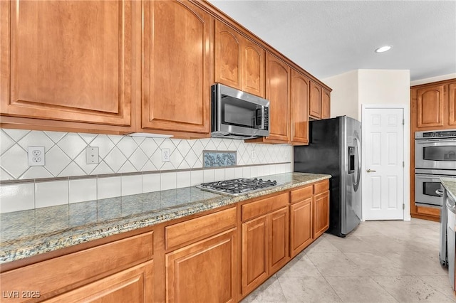 1155 Phillip Island St, Henderson, NV 89052 - kitchen with stainless steel appliances, light stone countertops, backsplash, brown cabinetry, and light tile patterned floors