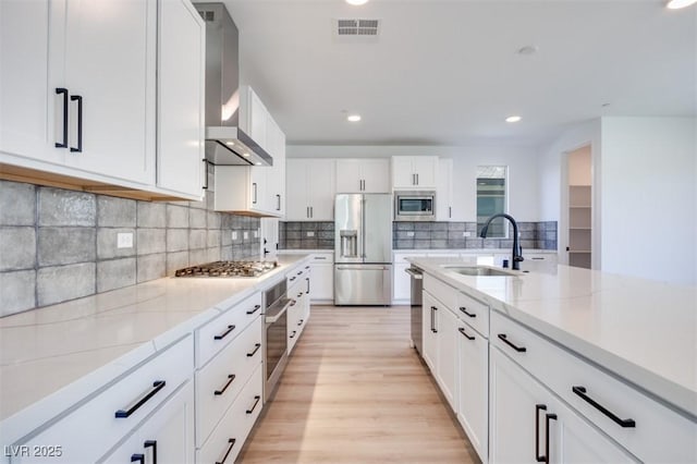 9265 Frazer St, Las Vegas, NV 89166 - kitchen featuring appliances with stainless steel finishes, wall chimney range hood, a sink, light wood finished floors, and white cabinets