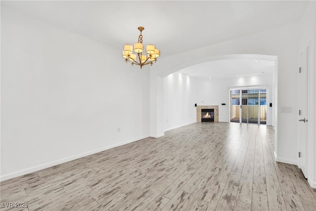 8725 W Flamingo Rd Unit 110, Las Vegas, NV 89147 - unfurnished living room featuring arched walkways, wood finished floors, a fireplace, a chandelier, and baseboards