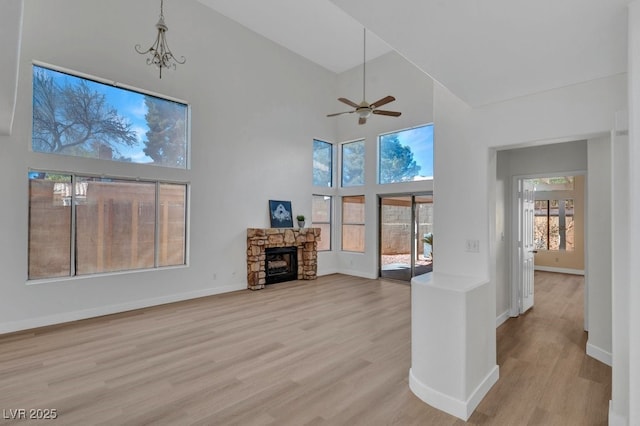 125 Firecreek Cir, Las Vegas, NV 89107 - unfurnished living room with a high ceiling, light wood finished floors, a ceiling fan, baseboards, and a stone fireplace