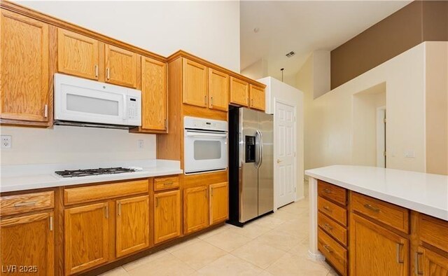 11204 Newbury Hills Ave, Las Vegas, NV 89138 - kitchen with white appliances, light countertops, light tile patterned flooring, brown cabinets, and high vaulted ceiling