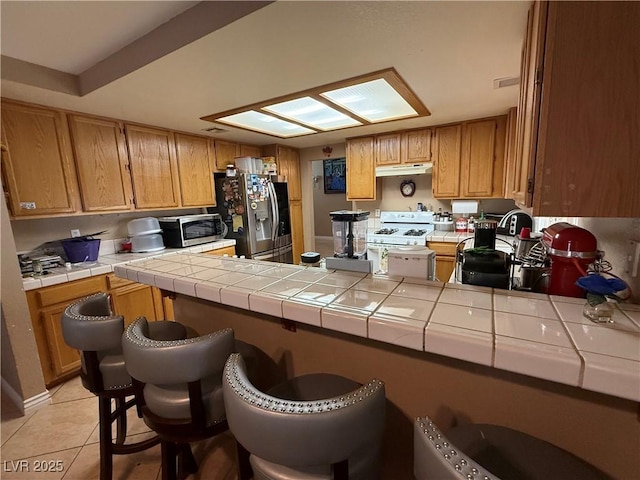 5517 Rock Creek Ln, Las Vegas, NV 89130 - kitchen featuring stainless steel appliances, a peninsula, tile countertops, light tile patterned floors, and under cabinet range hood