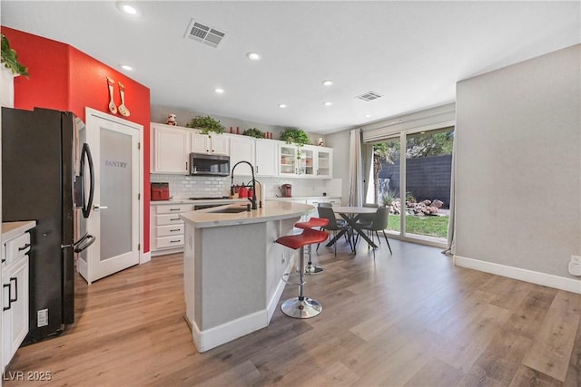 7821 Red Leaf Dr, Las Vegas, NV 89131 - kitchen with stainless steel microwave, black refrigerator with ice dispenser, recessed lighting, light wood-style flooring, and light countertops