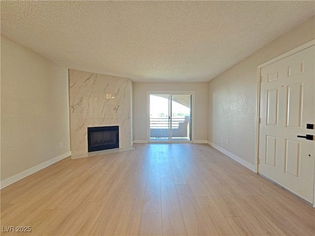 6853 Tamarus St Unit 202, Las Vegas, NV 89119 - unfurnished living room with a textured ceiling, light wood finished floors, a high end fireplace, and baseboards