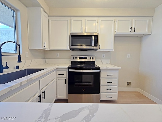 6853 Tamarus St Unit 202, Las Vegas, NV 89119 - kitchen featuring appliances with stainless steel finishes, a sink, white cabinetry, light stone counters, and light wood-style flooring