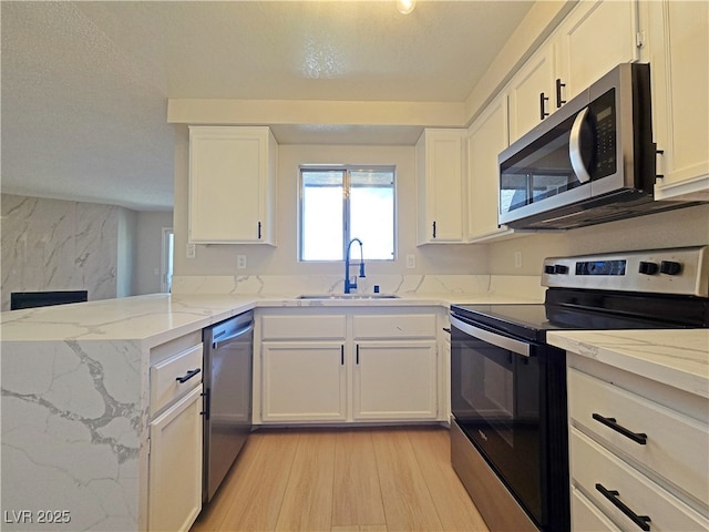 6853 Tamarus St Unit 202, Las Vegas, NV 89119 - kitchen with appliances with stainless steel finishes, a sink, light wood-type flooring, white cabinetry, and a textured ceiling