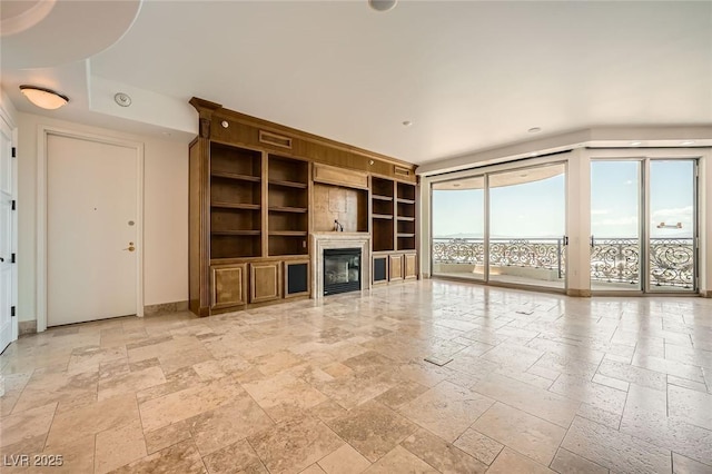 9101 Alta Dr Unit 1203, Las Vegas, NV 89145 - unfurnished living room featuring stone tile flooring, built in shelves, a glass covered fireplace, and baseboards