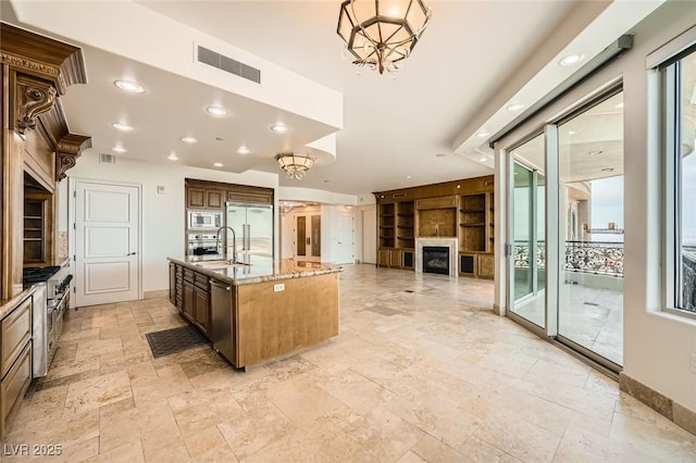 9101 Alta Dr Unit 1203, Las Vegas, NV 89145 - kitchen featuring built in appliances, stone tile floors, light stone counters, a fireplace, and a center island with sink