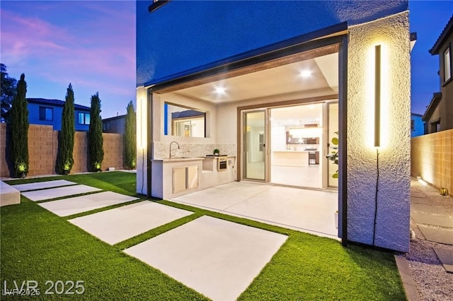 2407 Ridgeline Wash St, Las Vegas, NV 89138 - back of house at dusk featuring area for grilling, a fenced backyard, stucco siding, a patio area, and a sink