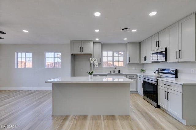 4360 El Tovar Rd, Las Vegas, NV 89115 - kitchen featuring appliances with stainless steel finishes, a sink, a center island, light wood-type flooring, and light countertops