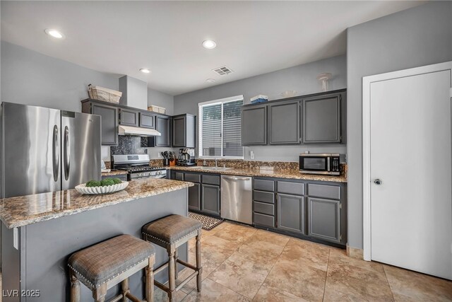 10952 Napa Ridge Dr, Las Vegas, NV 89144 - kitchen featuring stainless steel appliances, under cabinet range hood, light stone countertops, a kitchen bar, and a center island