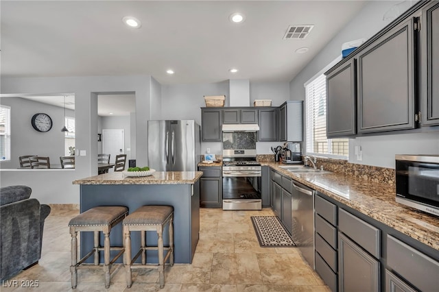 10952 Napa Ridge Dr, Las Vegas, NV 89144 - kitchen with appliances with stainless steel finishes, under cabinet range hood, a kitchen breakfast bar, a center island, and light stone countertops