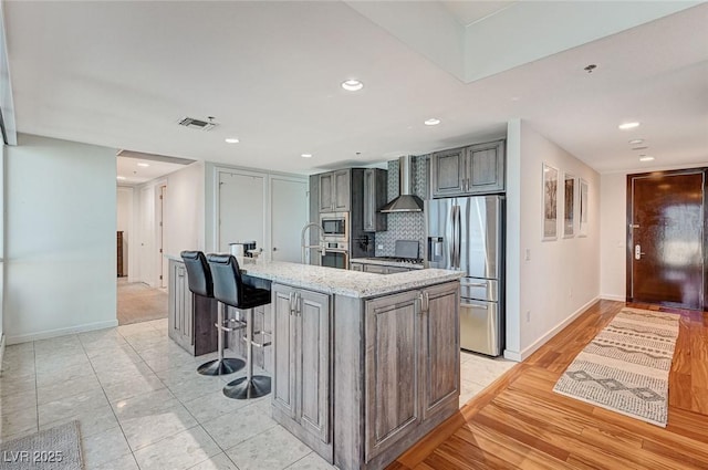 4525 Dean Martin Dr Unit 1208, Las Vegas, NV 89103 - kitchen featuring stainless steel appliances, wall chimney range hood, light stone counters, tasteful backsplash, and a large island
