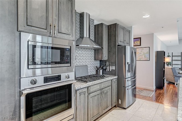 4525 Dean Martin Dr Unit 1208, Las Vegas, NV 89103 - kitchen with wall chimney range hood, appliances with stainless steel finishes, decorative backsplash, light tile patterned floors, and light stone counters