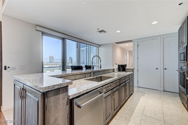4525 Dean Martin Dr Unit 1208, Las Vegas, NV 89103 - kitchen featuring appliances with stainless steel finishes, a kitchen island with sink, light stone countertops, recessed lighting, and dark brown cabinets