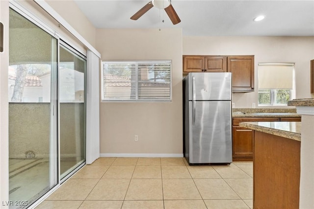 8409 Running Deer Ave Unit 203, Las Vegas, NV 89145 - kitchen featuring freestanding refrigerator, brown cabinetry, ceiling fan, light stone countertops, and light tile patterned floors