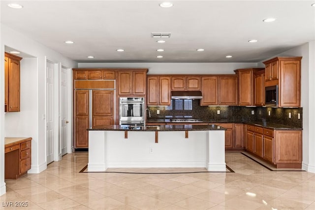 2846 Barrow Downs St, Las Vegas, NV 89135 - kitchen featuring under cabinet range hood, brown cabinetry, black microwave, dark stone counters, and a breakfast bar