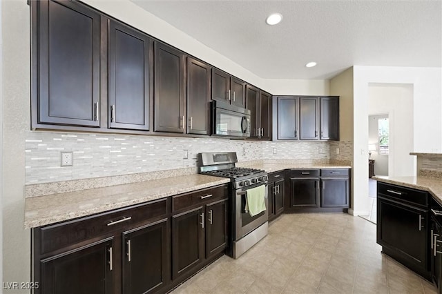 9104 Ashiwi Ave, Las Vegas, NV 89178 - kitchen featuring black microwave, stainless steel gas stove, tasteful backsplash, dark brown cabinets, and light stone countertops