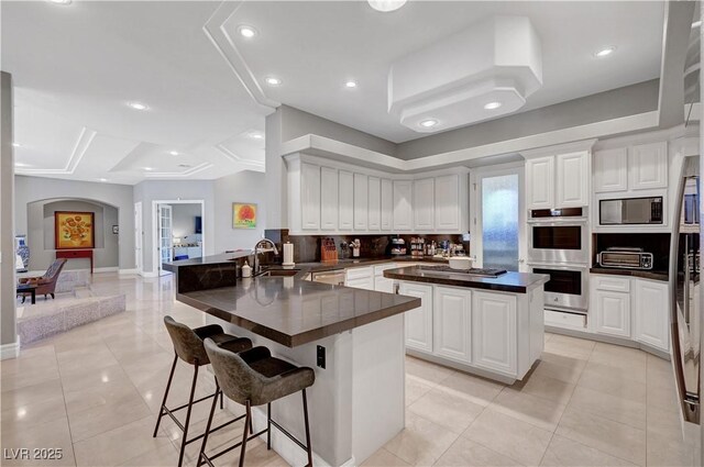 2111 Bogart Ct, Las Vegas, NV 89117 - kitchen with arched walkways, a sink, dark countertops, stainless steel appliances, and a peninsula