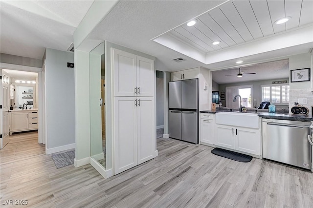 450 Intrepid Ct, Boulder City, NV 89005 - kitchen with stainless steel appliances, a tray ceiling, dark countertops, light wood-style floors, and white cabinetry