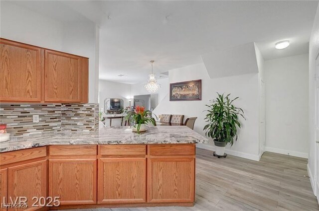 6320 Desert Leaf St Unit 101, North Las Vegas, NV 89081 - kitchen with tasteful backsplash, light stone counters, light wood finished floors, a peninsula, and baseboards