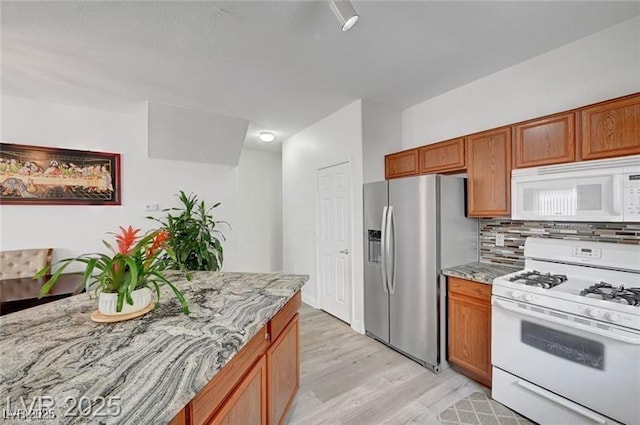 6320 Desert Leaf St Unit 101, North Las Vegas, NV 89081 - kitchen with white appliances, decorative backsplash, light wood-style flooring, and brown cabinetry