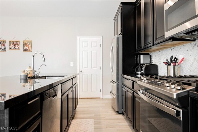 7002 Fossil Rim St, North Las Vegas, NV 89084 - kitchen with stainless steel appliances, a sink, decorative backsplash, light wood-style flooring, and dark cabinetry